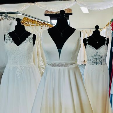 Three elegant white wedding dresses displayed on mannequins in a bridal shop.