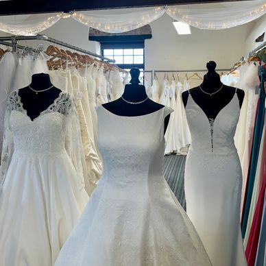 Three elegant white wedding dresses on black mannequins in a bridal shop.