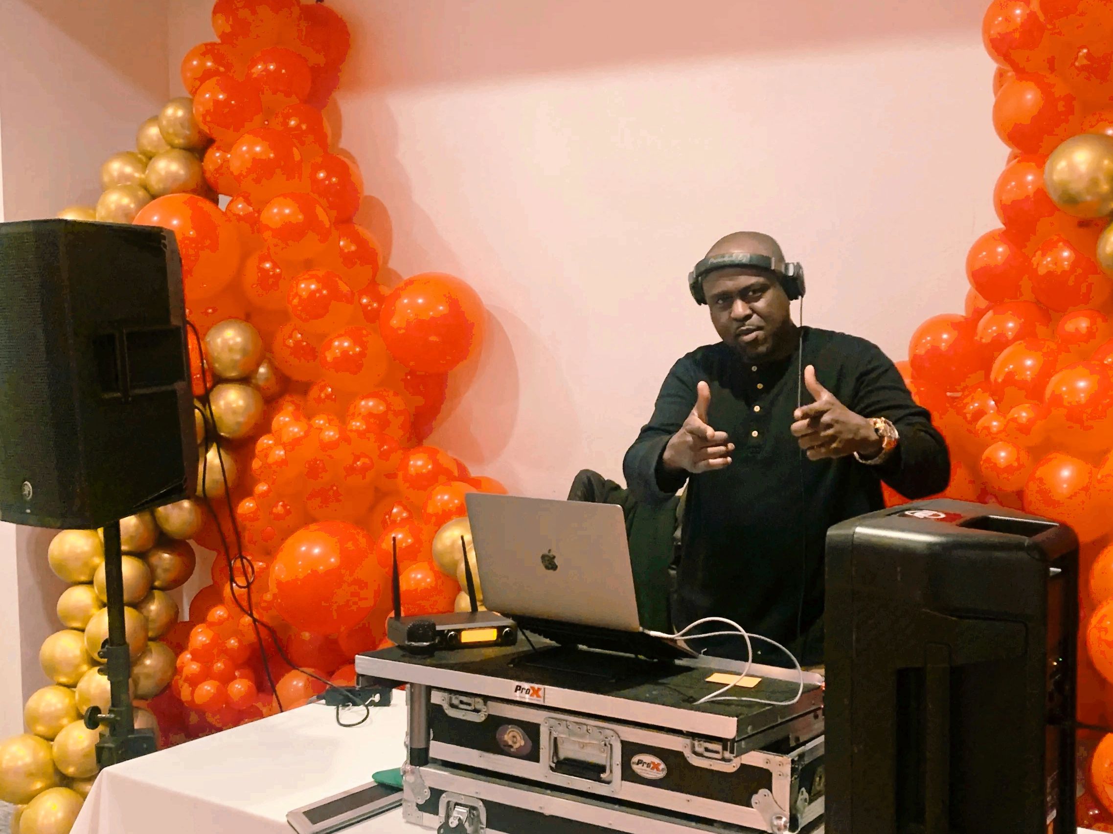 DJ playing music at a party with orange and gold balloon decorations.