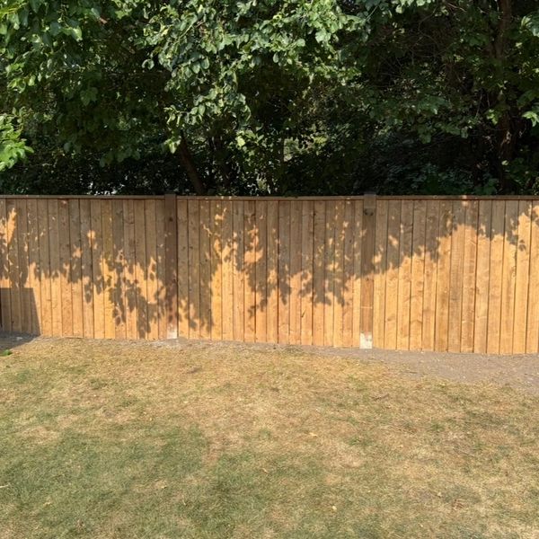 A wooden fence with tree shadows in a sunny backyard.