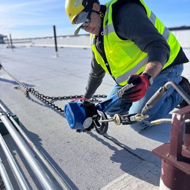 Construction worker in safety gear tightening a chain on a rooftop.