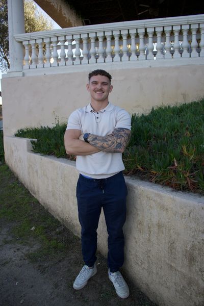 Smiling man with tattooed arm standing outdoors near a balustrade.