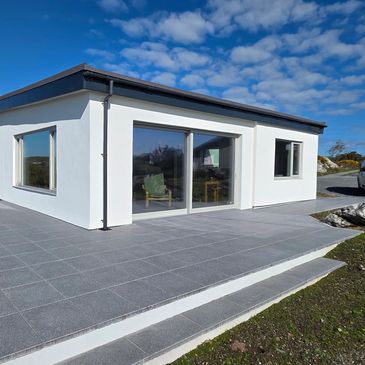 Modern white house with large windows and tiled patio under a blue sky.