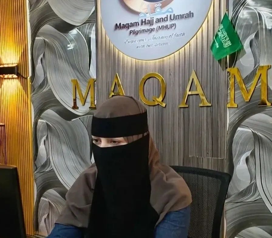 Woman in niqab sitting at a desk with Maqam Hajj and Umrah sign.