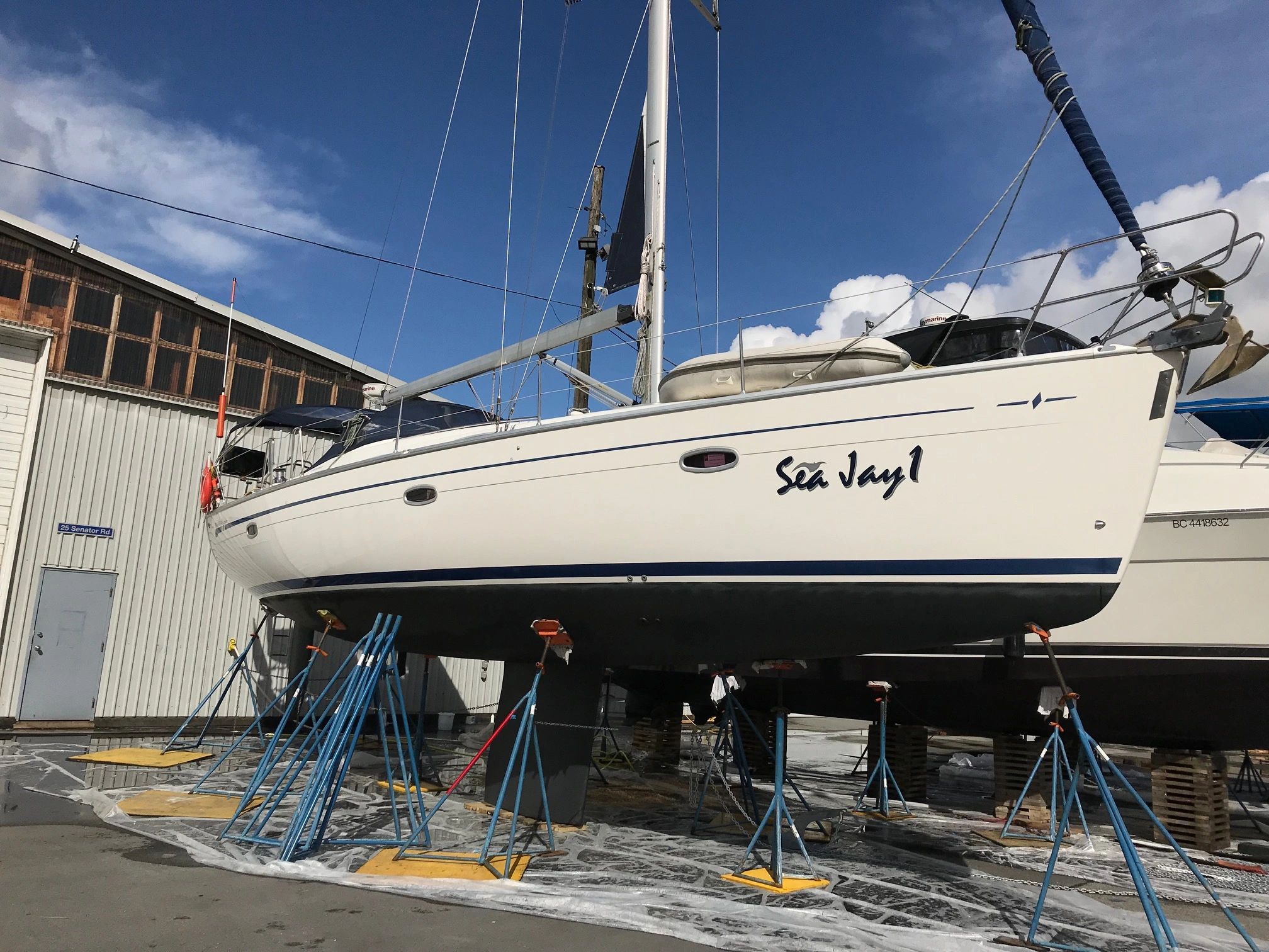 Sailboat named Sea Jay 1 on stands outside a building under a clear sky.