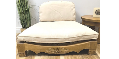 Low wooden chair with beige cushions and carved floral details.