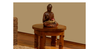 Wooden Buddha statue on a round wooden table with woven furniture nearby.