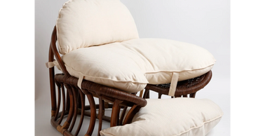 Cozy rattan chair with thick cream cushions on a white background.