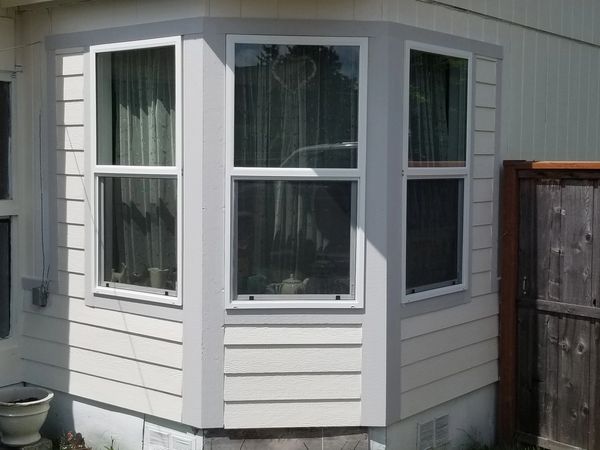A white bay window with curtains on a beige house exterior.