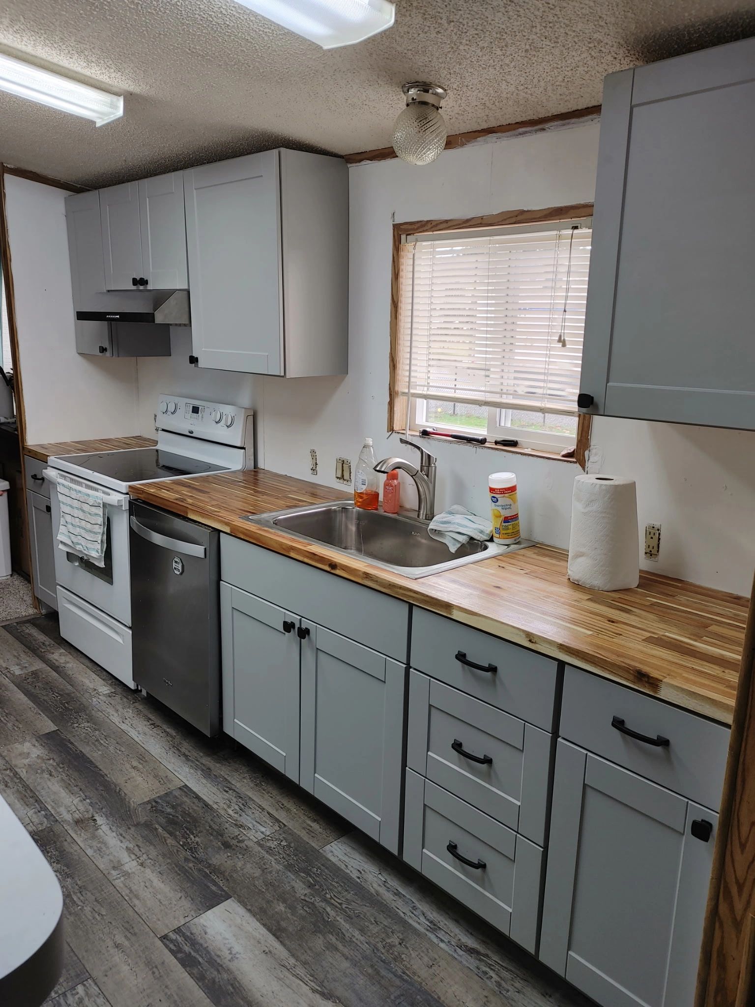 A modern kitchen with gray cabinets, wood countertops, and stainless steel appliances.