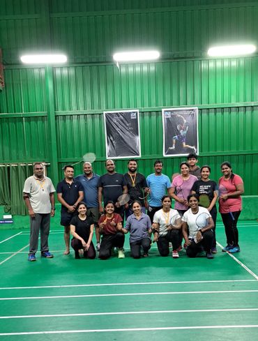 A group of badminton players posing on an indoor court with rackets and medals.
