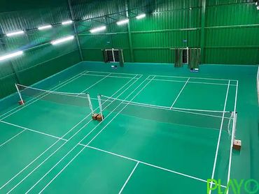 Indoor badminton court with green flooring and white lines under bright lights.