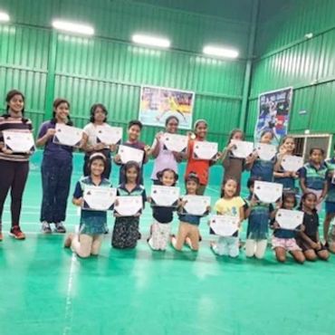 Group of girls holding certificates in a sports hall.