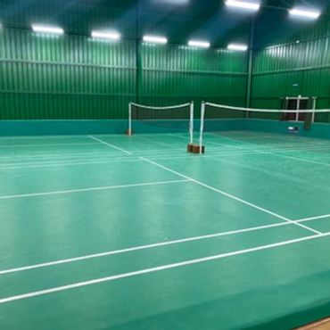 Indoor badminton court with green flooring and nets.