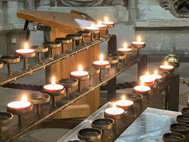 Lit votive candles on iron holders inside a church.