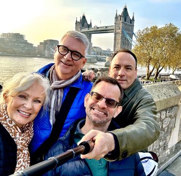 Four friends smiling for a selfie with Tower Bridge in London behind them.