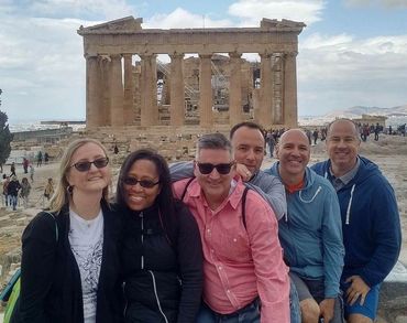 A group of friends posing happily in front of the Parthenon in Athens.