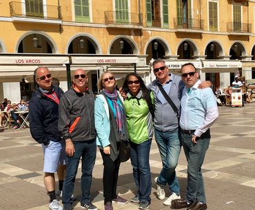 A group of six friends posing happily in a sunny European plaza.