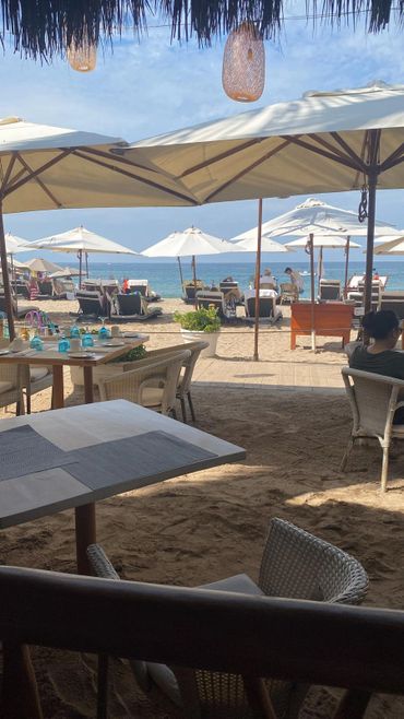 Beachside restaurant with tables and umbrellas overlooking the ocean.
