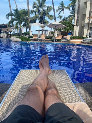 Relaxing by a blue pool under palm trees and umbrellas.