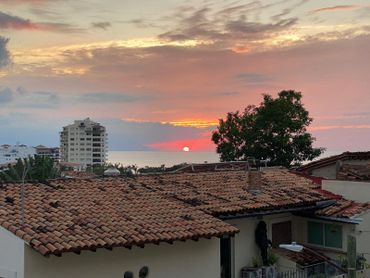 Sunset over tiled rooftops and ocean with a colorful sky.