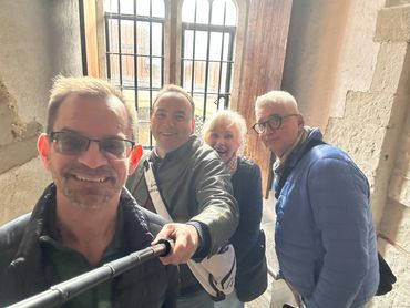 Four friends smiling and taking a selfie indoors near a window with iron bars.