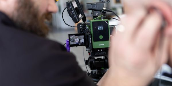 Person operating a professional video camera with a monitor showing the recording.