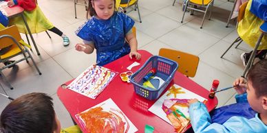 Children painting colorful pictures at a classroom table.