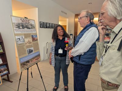 Three people discussing an informational display on a stand indoors.