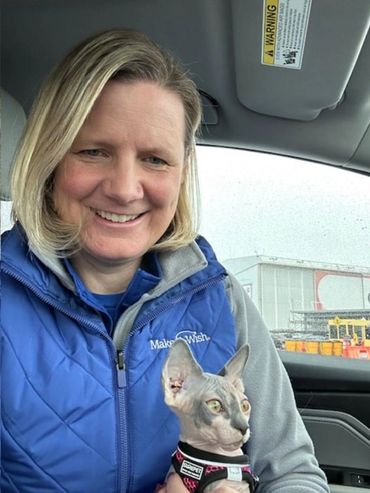 Woman in blue jacket holding a hairless cat inside a car.
