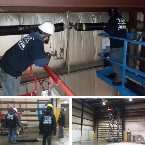 Technicians aligning a large commercial door with scissor lift coordination and safety gear.