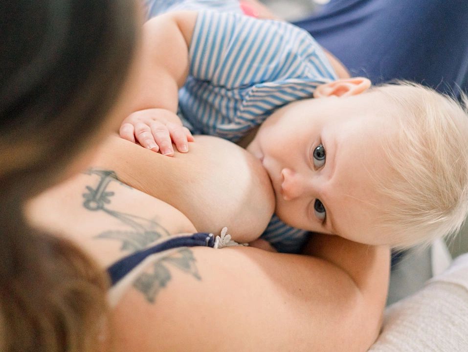 A baby breastfeeding while holding onto the mother's chest.