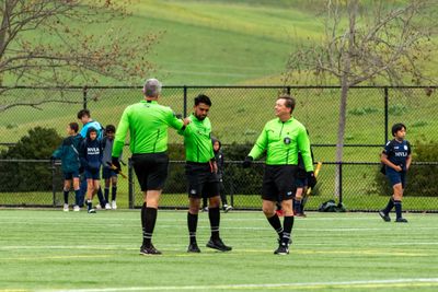 Soccer referees in green jerseys shaking hands on the field.