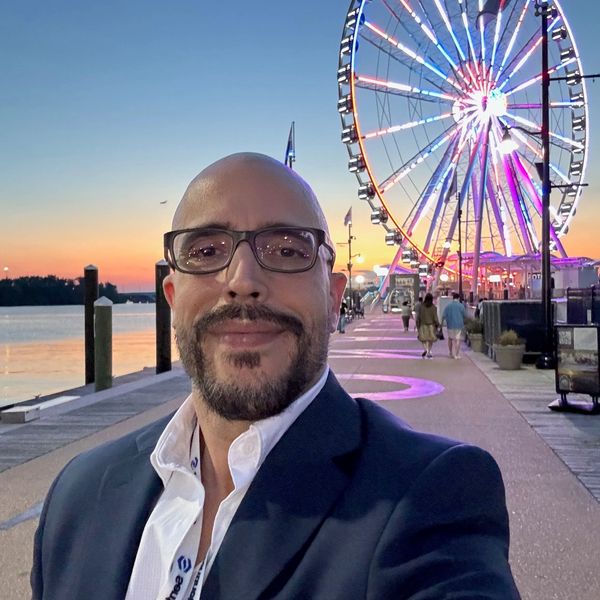 Man with glasses near a Ferris wheel at sunset.