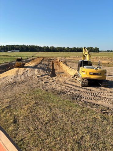 Excavators and bulldozer working on a large dirt excavation site under clear blue sky.
