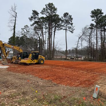 Construction site with heavy machinery and freshly graded red soil.