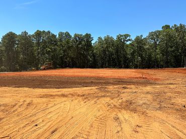 Cleared land with construction equipment and forest backdrop under blue sky.