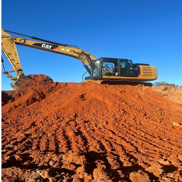A yellow CAT excavator on a mound of red soil under a clear blue sky.