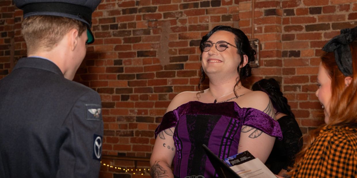 People socializing at a party with one person in a purple dress smiling.