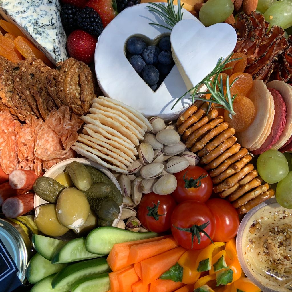 Colorful charcuterie board with assorted cheeses, crackers, fruits, nuts, and vegetables.