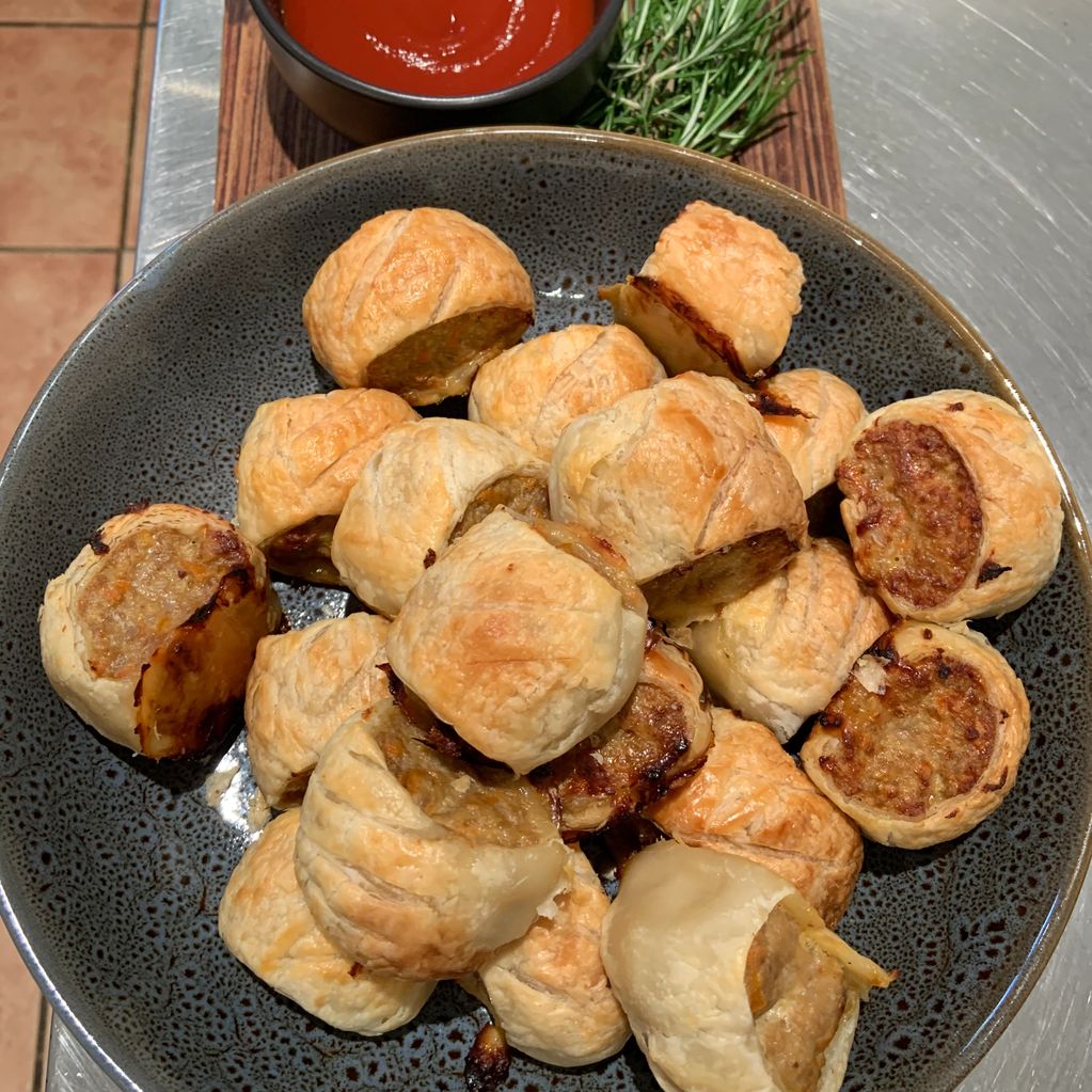 Golden sausage rolls served with ketchup and fresh rosemary.