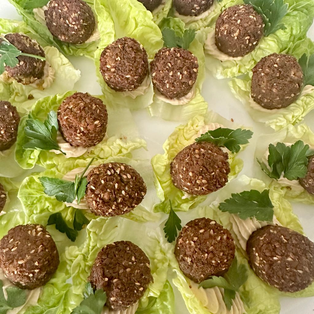 Falafel balls served on lettuce leaves with a dollop of hummus and parsley garnish.