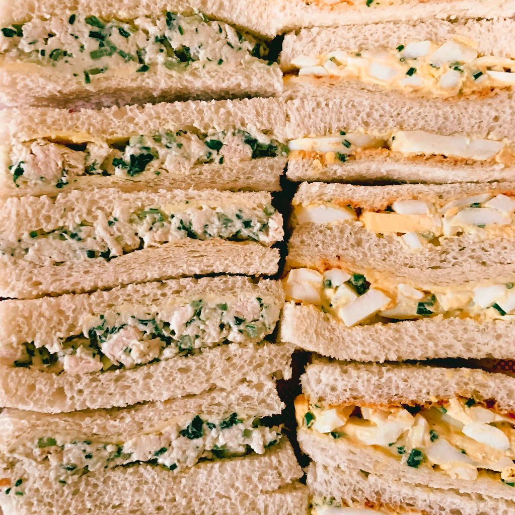 Close-up of various creamy sandwiches with herbs and egg filling.
