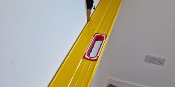 Yellow spirit level placed against a white wall for alignment checking.