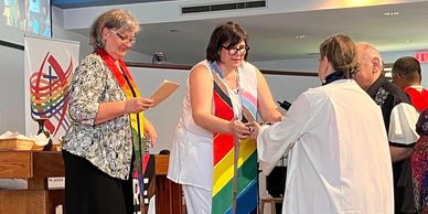 Carmen wearing inclusivity flag stole, leading in worship in Winnipeg, MB.