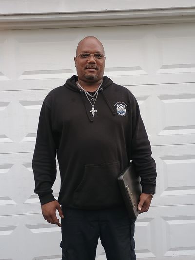 Man in black hoodie holding a laptop, standing in front of a white garage door.