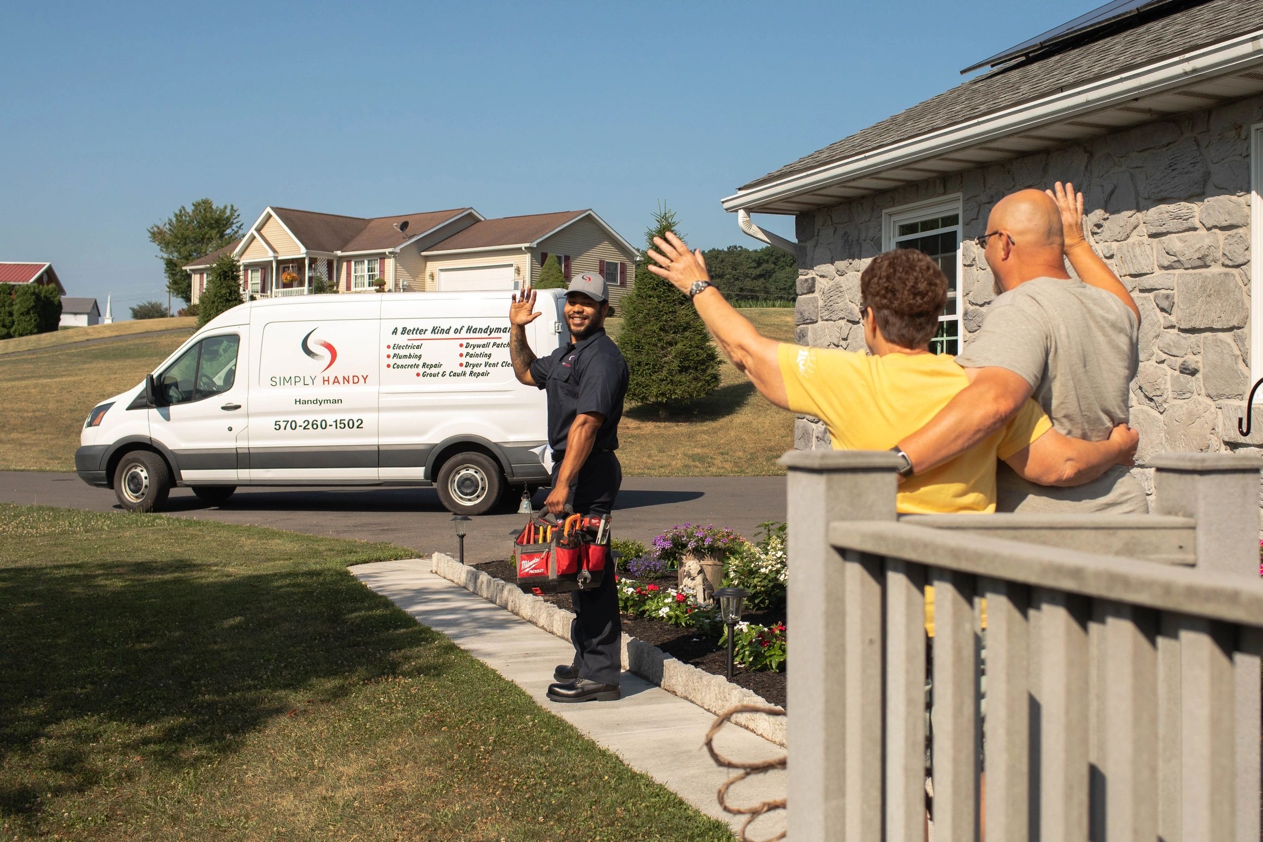 Handyman waving goodbye to a couple outside their home near a Simply Handy service van.