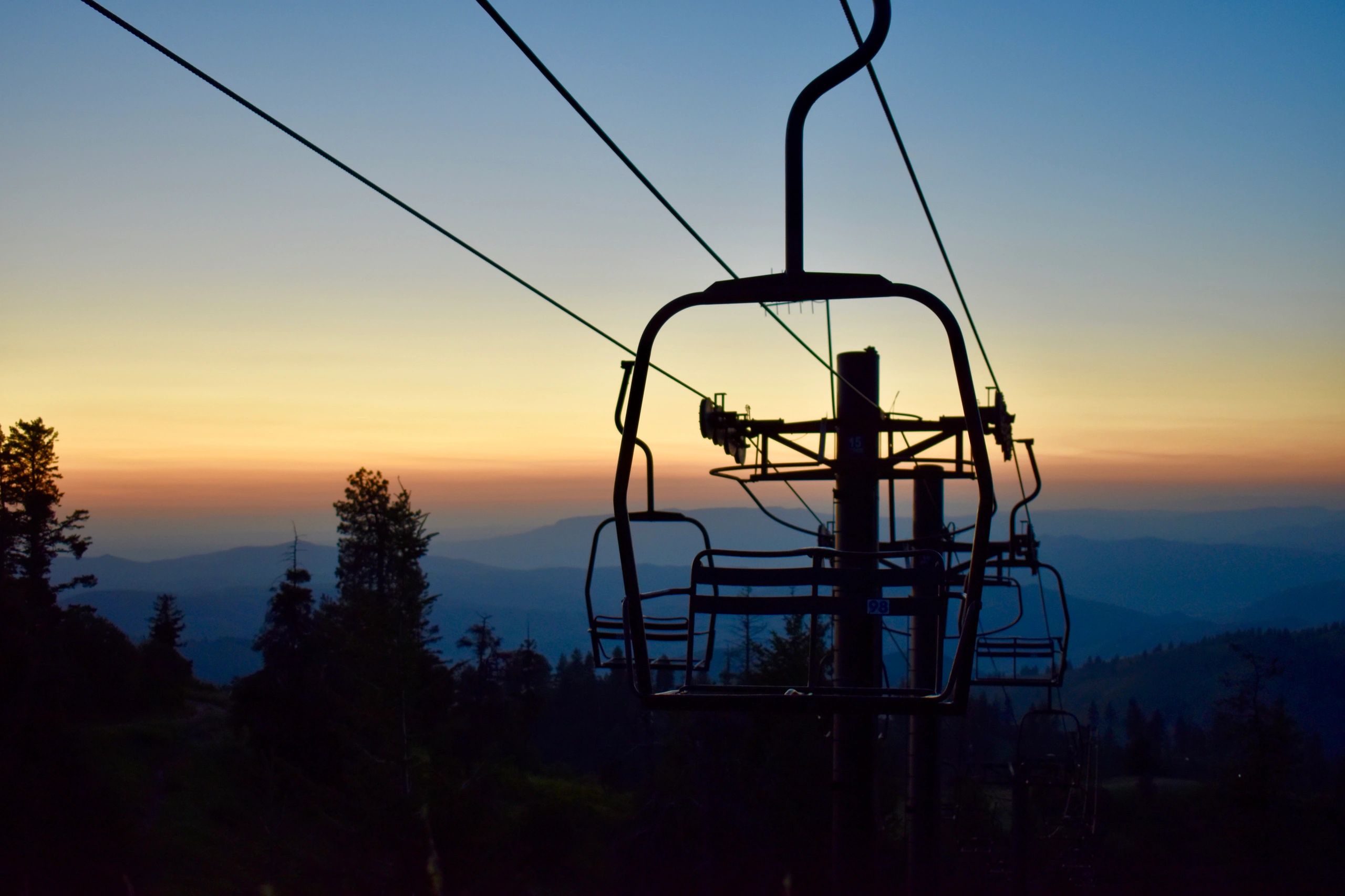 Silhouette of ski lift chairs at sunset over mountain landscape.