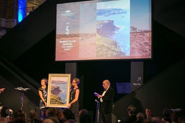 An auction displays Warrick Fuller's painting 'The Manly Ferry' to an audience.