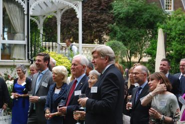 Group of people in formal attire holding drinks at an outdoor gathering.
